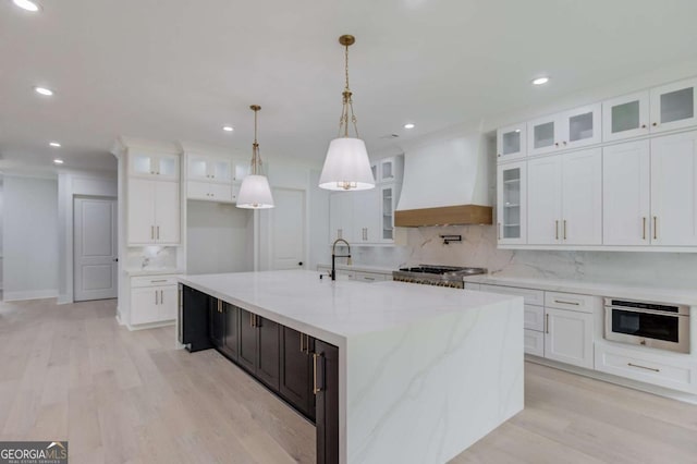 kitchen featuring a center island with sink, decorative backsplash, white cabinets, and premium range hood