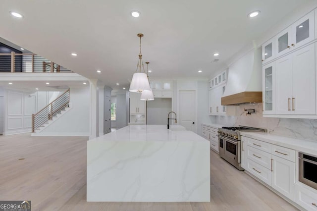 kitchen featuring light wood-type flooring, custom range hood, stainless steel appliances, white cabinets, and a large island