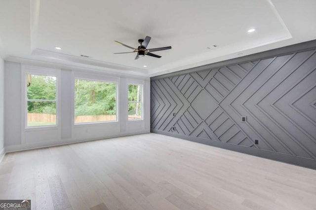 empty room featuring a tray ceiling, ceiling fan, and light hardwood / wood-style floors