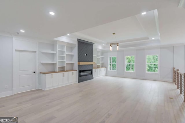 unfurnished living room featuring a fireplace, light hardwood / wood-style floors, and a tray ceiling