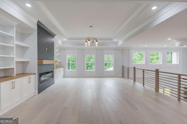 unfurnished living room featuring a raised ceiling, a chandelier, a fireplace, and light hardwood / wood-style floors