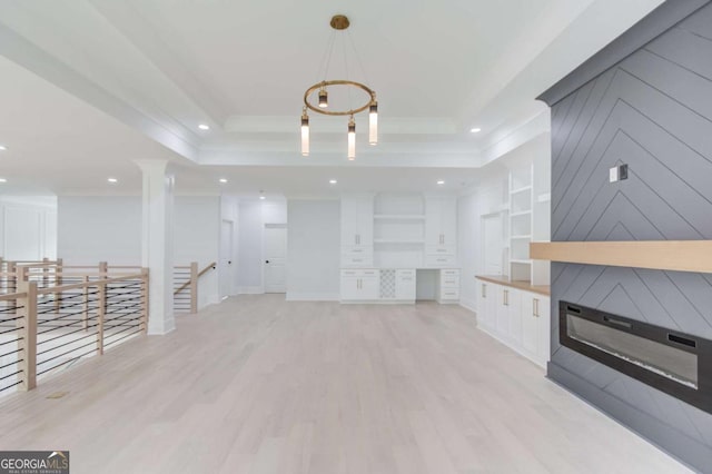 unfurnished living room featuring a large fireplace, ornamental molding, a tray ceiling, and light hardwood / wood-style flooring