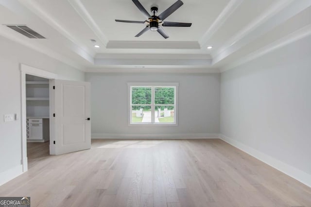 spare room featuring light wood-type flooring, a raised ceiling, and ceiling fan