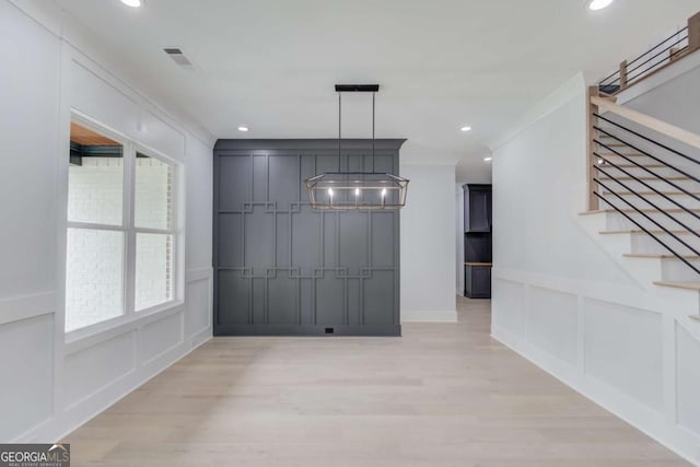 unfurnished dining area featuring light hardwood / wood-style floors, an inviting chandelier, and ornamental molding