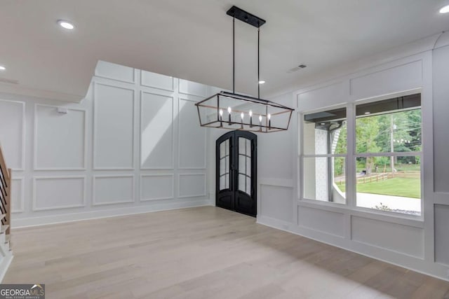 unfurnished dining area with light hardwood / wood-style floors, french doors, and a chandelier