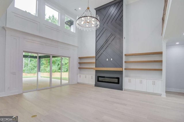 unfurnished living room featuring a large fireplace, light hardwood / wood-style flooring, plenty of natural light, and a notable chandelier