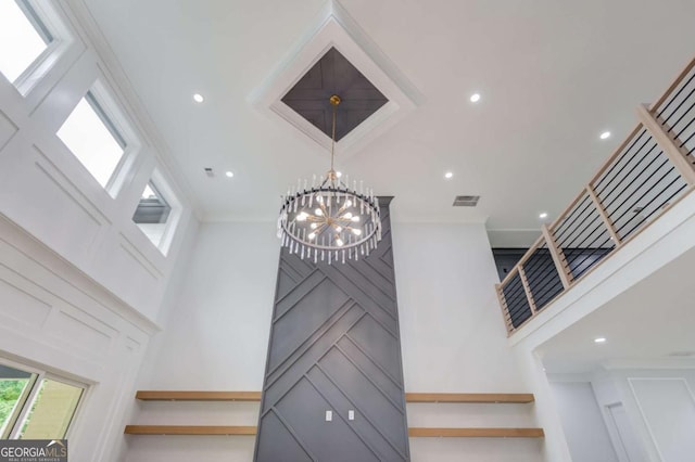 stairway featuring crown molding, a towering ceiling, and a notable chandelier