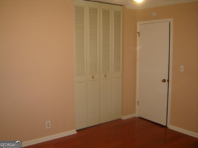 unfurnished bedroom with wood-type flooring, crown molding, and a closet