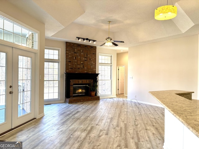 unfurnished living room featuring a wealth of natural light, french doors, wood-type flooring, and a brick fireplace