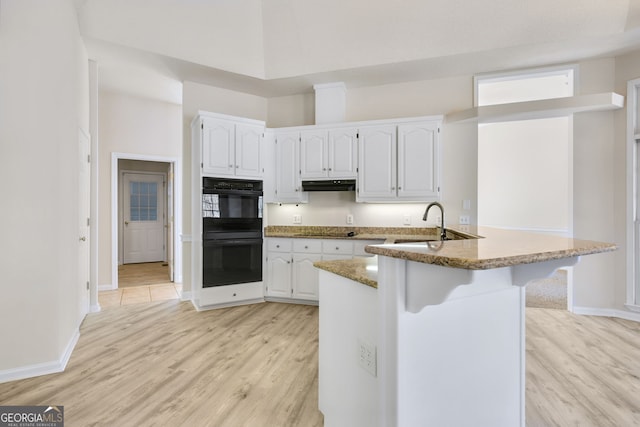 kitchen featuring black appliances, sink, kitchen peninsula, light hardwood / wood-style floors, and white cabinetry