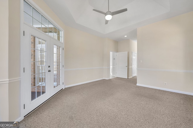 empty room with a tray ceiling, ceiling fan, french doors, and carpet floors