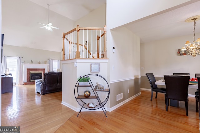 dining room featuring a fireplace, light wood-type flooring, high vaulted ceiling, and ceiling fan with notable chandelier