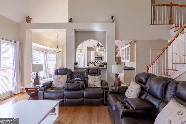 living room featuring ceiling fan with notable chandelier, high vaulted ceiling, and light hardwood / wood-style flooring