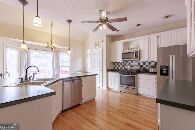 kitchen featuring decorative light fixtures, white cabinetry, stainless steel appliances, and vaulted ceiling