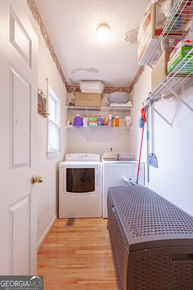 clothes washing area featuring washer and clothes dryer, light hardwood / wood-style flooring, and a textured ceiling