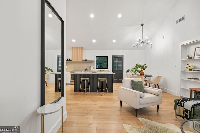 living room featuring built in shelves, high vaulted ceiling, light hardwood / wood-style floors, and a notable chandelier