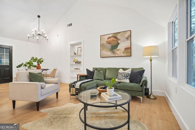 living room with a notable chandelier, built in shelves, high vaulted ceiling, and light hardwood / wood-style flooring