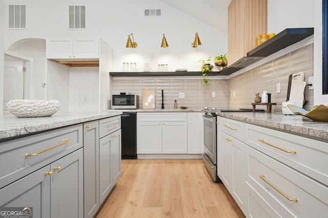 kitchen with decorative backsplash, appliances with stainless steel finishes, light stone countertops, white cabinets, and light hardwood / wood-style floors