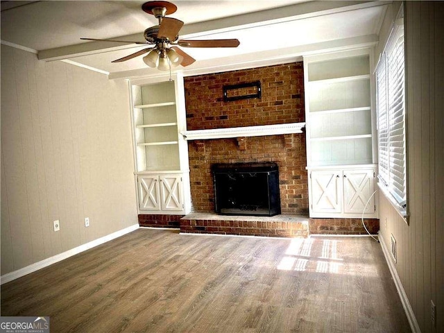 unfurnished living room featuring built in shelves, ceiling fan, wood-type flooring, beam ceiling, and a fireplace