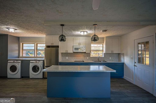 kitchen featuring white cabinets, independent washer and dryer, hanging light fixtures, and a wealth of natural light