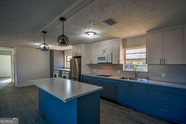 kitchen with sink, a center island, washing machine and dryer, stainless steel fridge, and pendant lighting