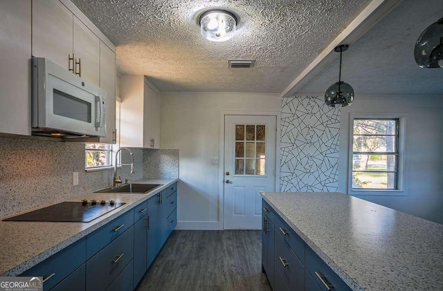 kitchen featuring black electric stovetop, dark wood-type flooring, sink, blue cabinetry, and decorative light fixtures