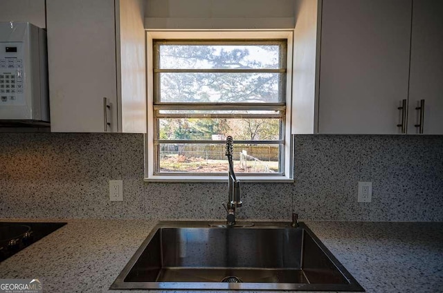 kitchen with decorative backsplash, light stone countertops, a healthy amount of sunlight, and sink