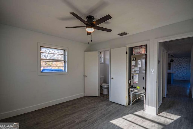 unfurnished bedroom featuring heating unit, ceiling fan, dark hardwood / wood-style flooring, and ensuite bathroom