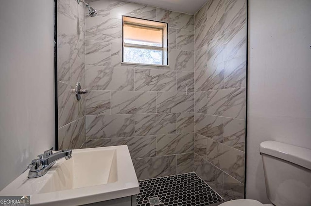 bathroom with a tile shower, toilet, and sink