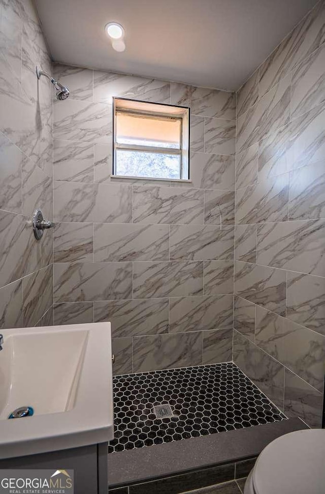 bathroom featuring a tile shower, vanity, and toilet