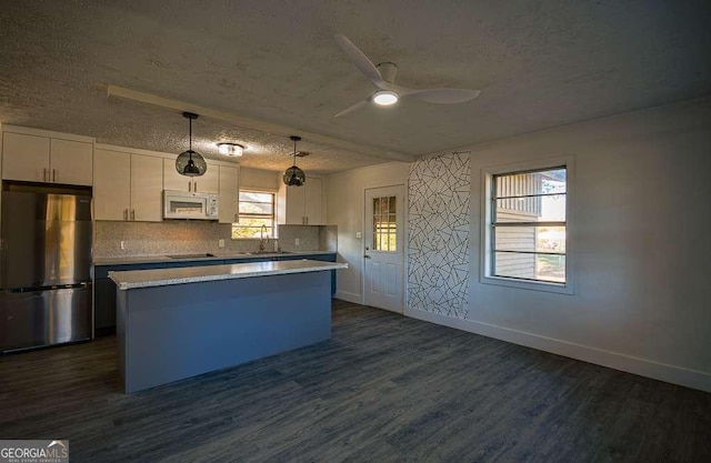 kitchen with decorative light fixtures, white cabinetry, sink, and stainless steel refrigerator