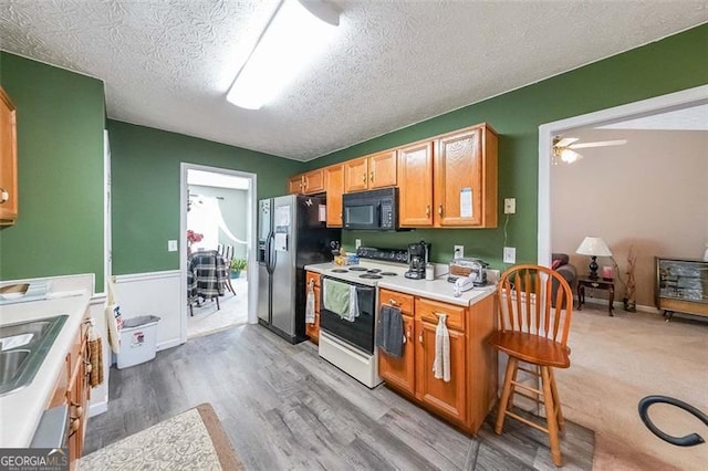 kitchen featuring stainless steel refrigerator with ice dispenser, a textured ceiling, ceiling fan, electric stove, and light hardwood / wood-style flooring