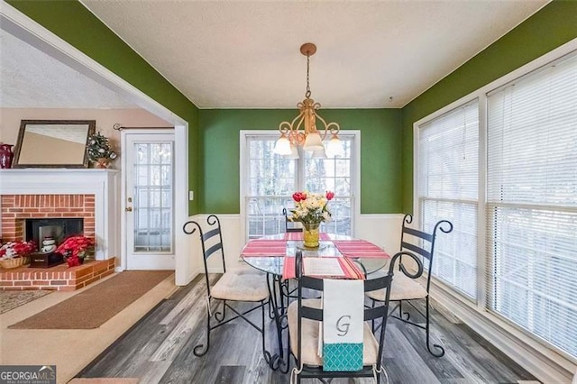 dining room featuring a brick fireplace, a textured ceiling, dark wood-type flooring, and a chandelier