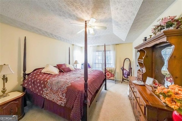 bedroom featuring light carpet, a textured ceiling, a tray ceiling, and ceiling fan