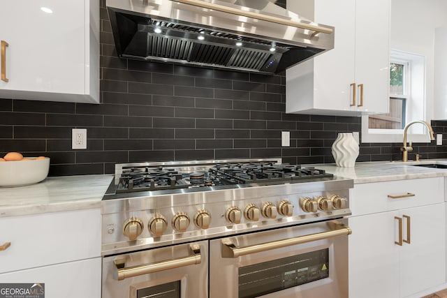 kitchen featuring wall chimney exhaust hood, double oven range, white cabinetry, and tasteful backsplash