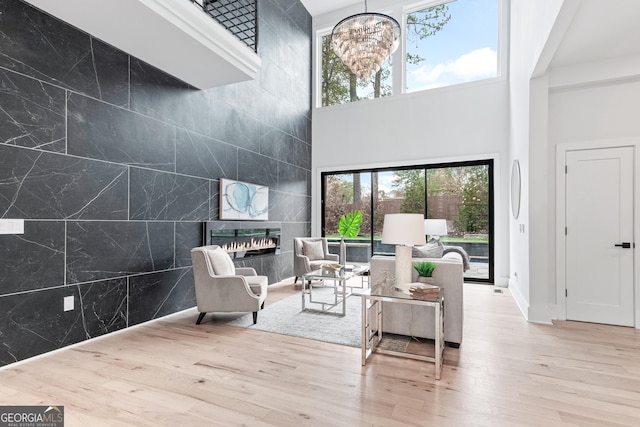 living room featuring a towering ceiling, a chandelier, a tiled fireplace, tile walls, and light wood-type flooring