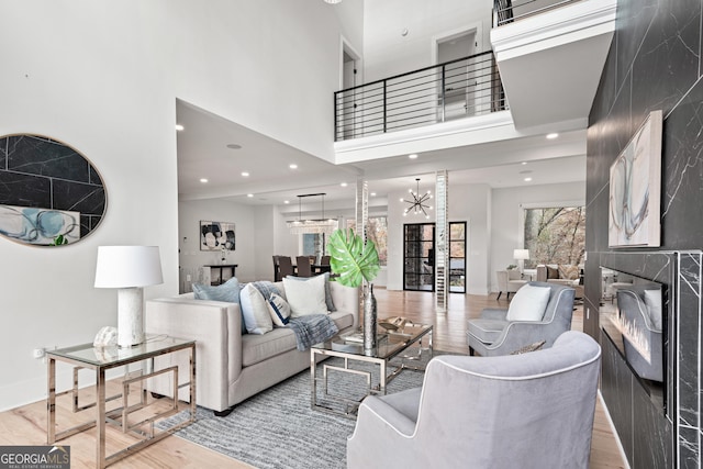 living room featuring light wood-type flooring, a towering ceiling, a chandelier, and a fireplace