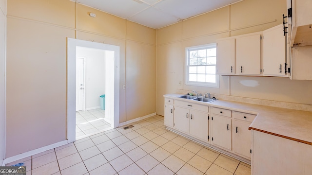 kitchen featuring white cabinets, range hood, light tile patterned flooring, and sink