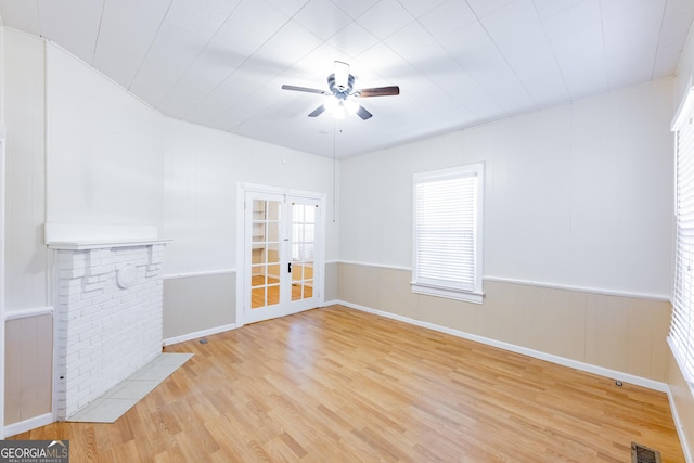 unfurnished living room featuring a fireplace, french doors, light wood-type flooring, and ceiling fan