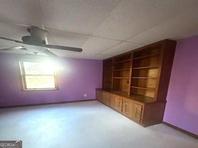 interior space featuring built in shelves, ceiling fan, and a drop ceiling