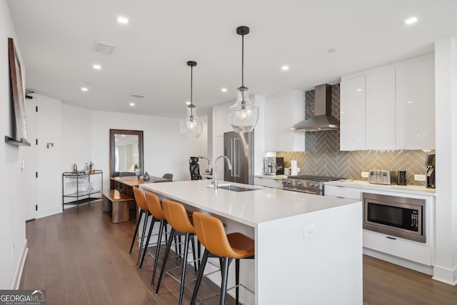 kitchen with pendant lighting, premium appliances, an island with sink, and wall chimney range hood