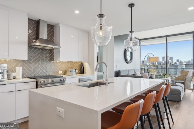 kitchen with wall chimney exhaust hood, a kitchen island with sink, decorative light fixtures, and light hardwood / wood-style flooring