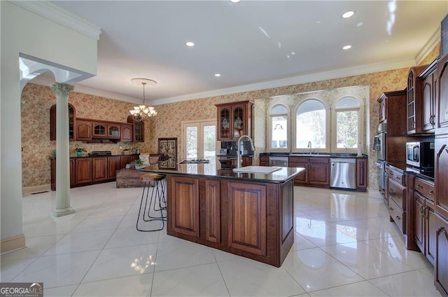 kitchen featuring ornate columns, sink, stainless steel appliances, crown molding, and a kitchen island with sink