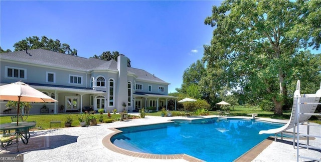 view of swimming pool with a lawn, a diving board, a water slide, and a patio