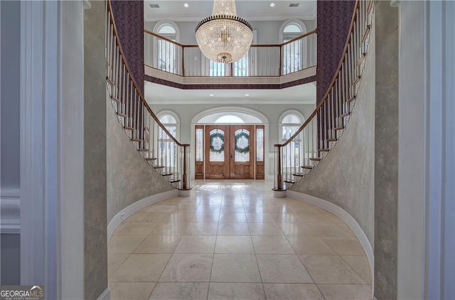 entryway with a high ceiling, ornamental molding, french doors, and a notable chandelier