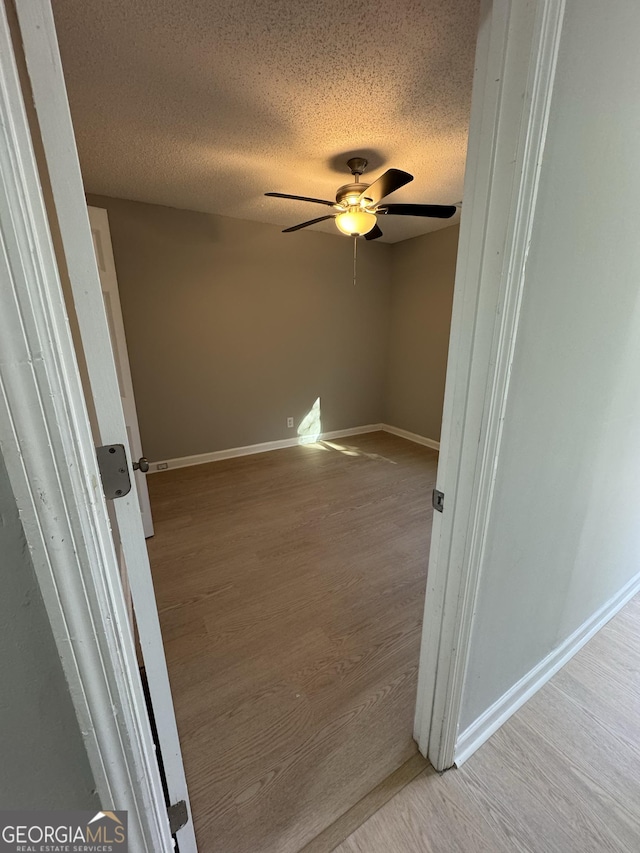 unfurnished room with ceiling fan, light wood-type flooring, and a textured ceiling