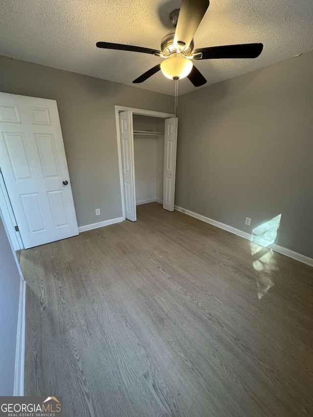 unfurnished bedroom with ceiling fan, a closet, a textured ceiling, and hardwood / wood-style flooring