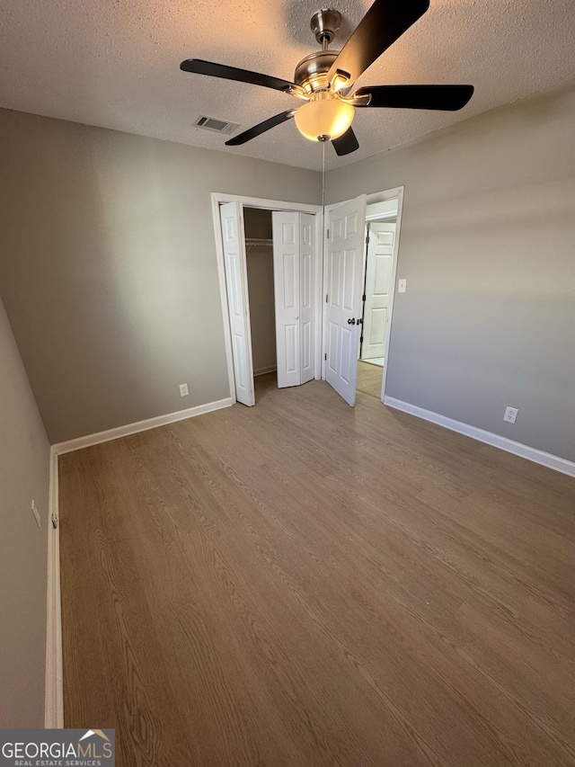 unfurnished bedroom with ceiling fan, a closet, wood-type flooring, and a textured ceiling