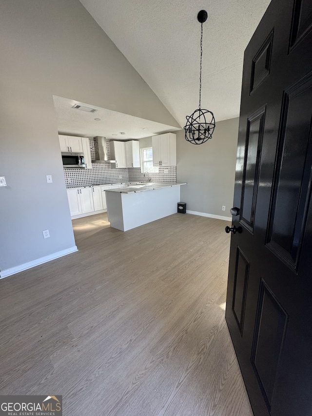 kitchen with pendant lighting, white cabinets, wall chimney exhaust hood, tasteful backsplash, and light hardwood / wood-style floors