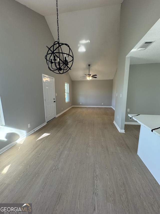 unfurnished dining area featuring hardwood / wood-style flooring, ceiling fan with notable chandelier, and high vaulted ceiling